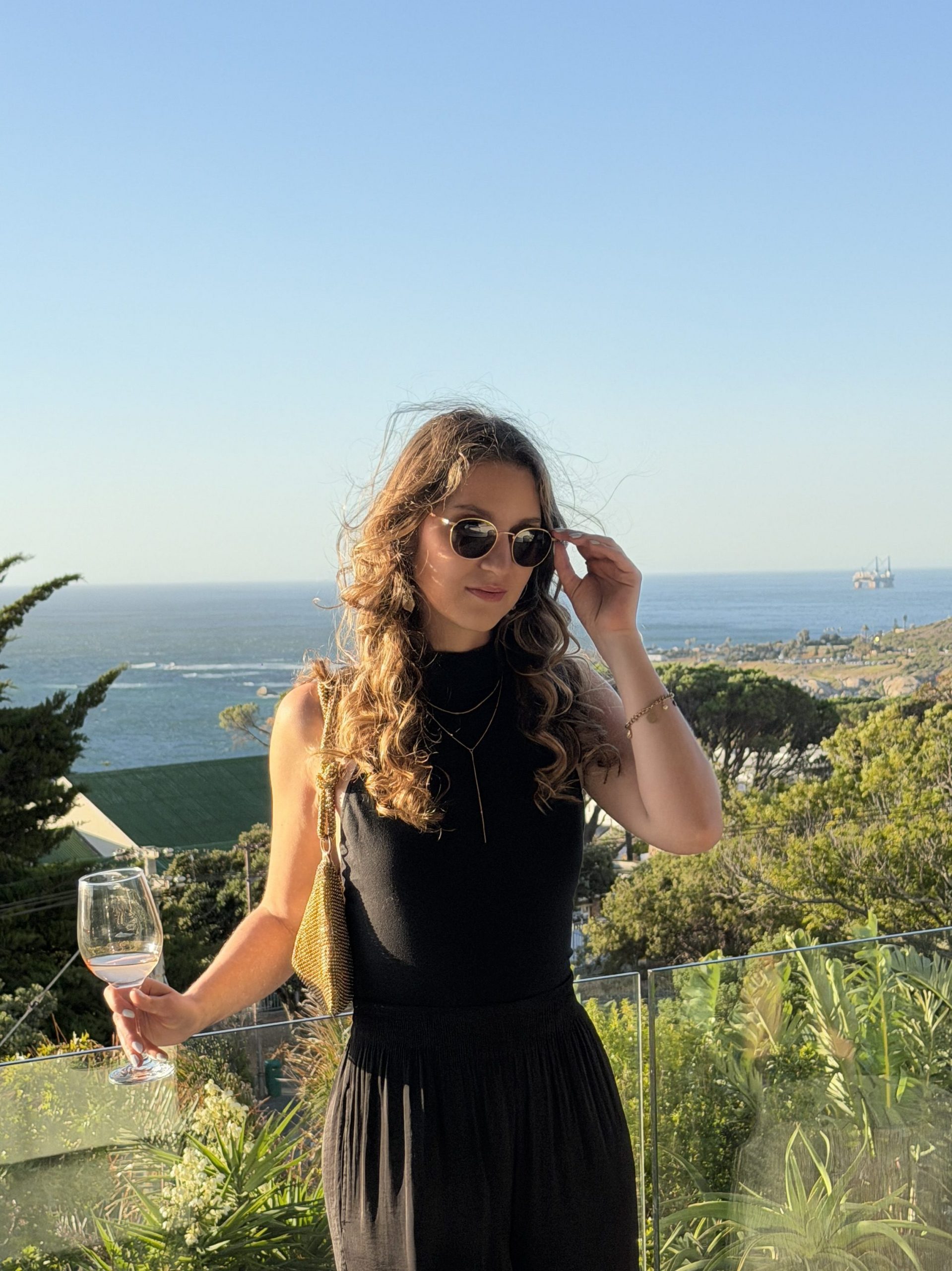 Frau mit Weinglas bei Sonnenuntergang mit Blick aufs Meer in Kapstadt